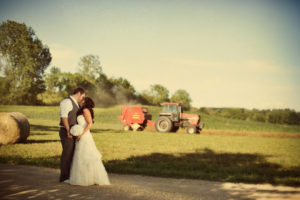 A bride and groom kiss in front of a tractor.