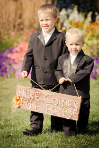 Two boys in suits holding a sign that says here comes the bride.