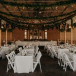 A wedding reception set up with white tables and greenery.