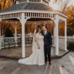 A bride and groom standing in front of a gazebo at sunset.