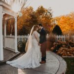 A bride and groom standing in front of a gazebo in the fall.