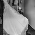 A black and white photo of a wedding dress hanging in a mirror.