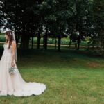 A bride standing in a field with trees in the background.