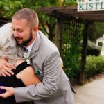 A man and woman hugging in front of a sign.