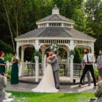 A bride and groom kiss in front of a gazebo.