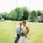 A bride and groom sitting on a swing in a field.