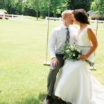 A bride and groom sitting on a swing in a field.