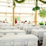 A wedding reception in a greenhouse with white tables and chairs.