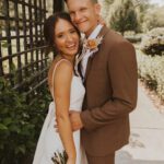 A bride and groom posing for a photo in front of a pergola.