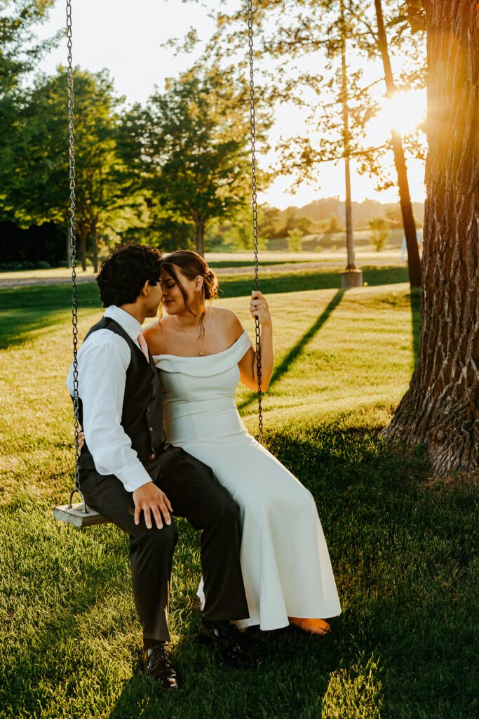 A bride and groom sitting on a swing at sunset.