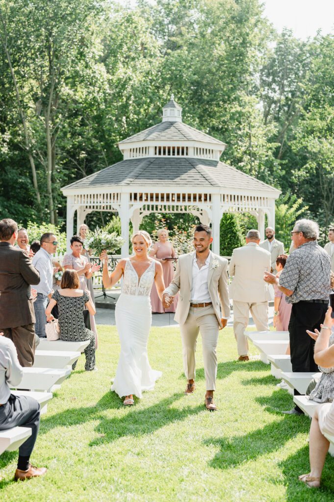 A bride and groom walking down the aisle at an outdoor wedding.