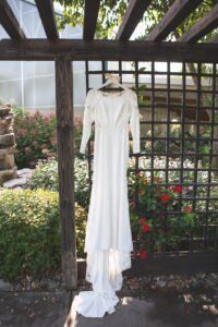 A white wedding dress hanging on a pergola.