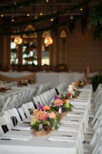 A long table set with white chairs and flowers.