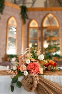 A table with flowers and a tan tablecloth.