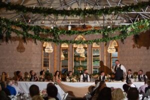 A wedding reception in a large room with greenery hanging from the ceiling.