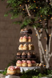 Three tiers of cupcakes on a table in front of a tree.